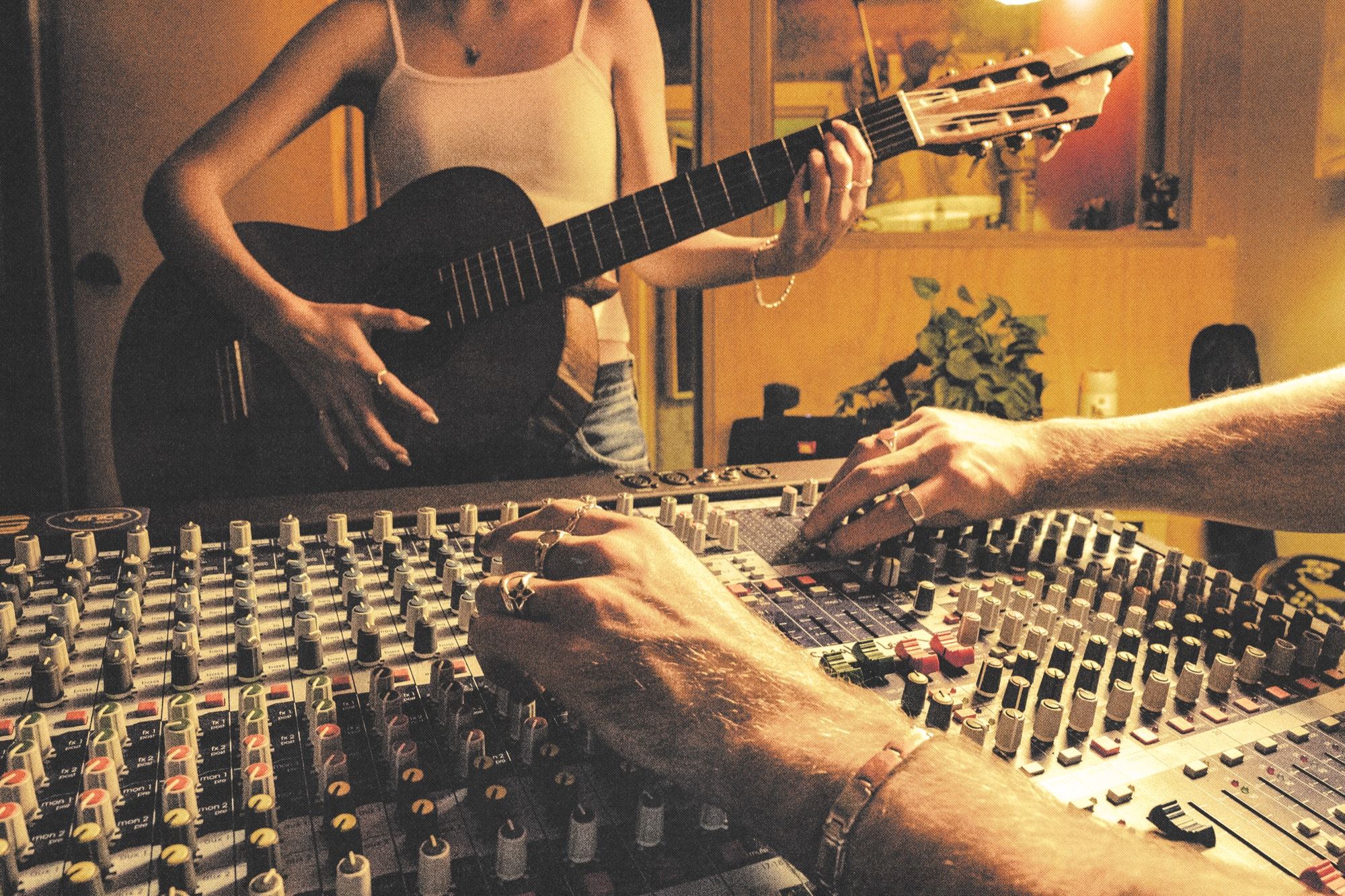 Hands on a mixing desk wearing rings; a guitar behind